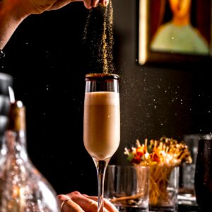 bar tender sprinkles golden glitter into cocktail in champagne glass
