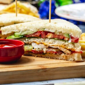 side view club sandwich with grilled chicken tomato cucumber lettuce mayo ketchup and french fries on a board